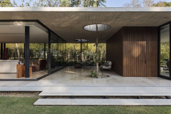 La vivienda Garafulic consta con un terreno privilegiado rodeado de vegetación que está situado en una urbanización cerrada en la zona del Urubó. La topografía natural del terreno permite que la volumetría de la casa se apoye en el punto más alto del mismo, aprovechando así los desniveles para poder generar una planta de servicio en el subsuelo. Esto nos permite resolver el programa de la vivienda en 3 niveles, pero al mismo tiempo mantener una composición de dos volúmenes que se solapan y se posan sobre el terreno natural.

El acceso principal nos dirige hacia la planta baja, la que está resuelta bajo el concepto de `planta libre´. Diferentes áreas de servicio como el sauna, la escalera principal,  el shaft, la despensa y  la vinoteca; funcionan como volúmenes de separación y actúan como colchones entre los distintos programas. Con el fin de no generar habitaciones cerradas, la planta baja genera un espacio en común cuyas divisiones crean una fragmentación del espacio entre los distintos programas sin afectar la circulación libre

El recibidor o hall funciona como un distribuidor entre el family room y el pasillo principal, que nos lleva al cuarto de huéspedes, la cocina o el living comedor.  Entre el living-comedor y el gimnasio podemos apreciar una galería que nos lleva a una cubierta verde que mira hacia el patio interior y la piscina.

En el segundo piso contamos con el estar familiar y dos habitaciones en suite. La habitación principal cuenta con una pequeña terraza que aprovecha las mejores vistas del terreno hacia un pequeño bosque localizado al frente del mismo.