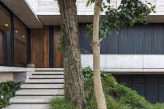 La vivienda Garafulic consta con un terreno privilegiado rodeado de vegetación que está situado en una urbanización cerrada en la zona del Urubó. La topografía natural del terreno permite que la volumetría de la casa se apoye en el punto más alto del mismo, aprovechando así los desniveles para poder generar una planta de servicio en el subsuelo. Esto nos permite resolver el programa de la vivienda en 3 niveles, pero al mismo tiempo mantener una composición de dos volúmenes que se solapan y se posan sobre el terreno natural.

El acceso principal nos dirige hacia la planta baja, la que está resuelta bajo el concepto de `planta libre´. Diferentes áreas de servicio como el sauna, la escalera principal,  el shaft, la despensa y  la vinoteca; funcionan como volúmenes de separación y actúan como colchones entre los distintos programas. Con el fin de no generar habitaciones cerradas, la planta baja genera un espacio en común cuyas divisiones crean una fragmentación del espacio entre los distintos programas sin afectar la circulación libre

El recibidor o hall funciona como un distribuidor entre el family room y el pasillo principal, que nos lleva al cuarto de huéspedes, la cocina o el living comedor.  Entre el living-comedor y el gimnasio podemos apreciar una galería que nos lleva a una cubierta verde que mira hacia el patio interior y la piscina.

En el segundo piso contamos con el estar familiar y dos habitaciones en suite. La habitación principal cuenta con una pequeña terraza que aprovecha las mejores vistas del terreno hacia un pequeño bosque localizado al frente del mismo.